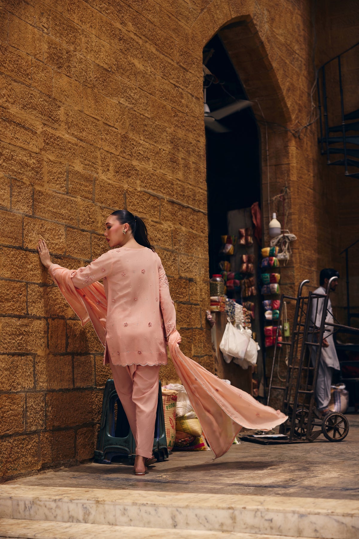 Model in Coronation Pink at a sandstone wall, the peach silk dupatta flowing behind her