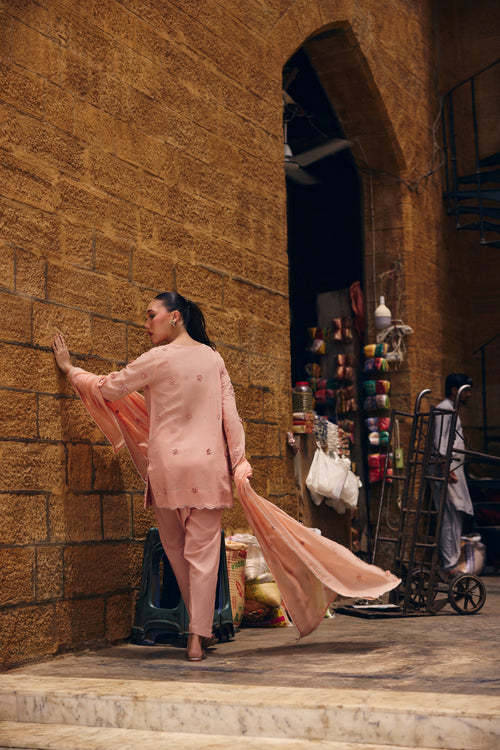 Model in Coronation Pink at a sandstone wall, the peach silk dupatta flowing behind her